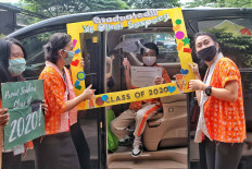 A student poses with his graduation certificate while his teachers congratulate him on June 15, during a drive-thru moving up ceremony in South Tangerang, Banten. JP/Seto Wardhana