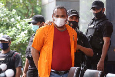 A Jakarta Police officer escorts gang leader John Refra (center), also known as John Kei, to a press conference at the Jakarta Police headquarters on June 22. John was arrested on June 21 for allegedly masterminding attacks and a murder in West Jakarta and Tangerang, Banten. JP/Dhoni Setiawan