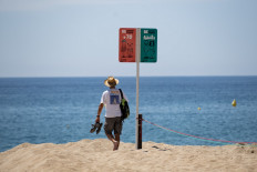 A man walks past a sign showing age-designated areas on a beach in Lloret de Mar on June 22, 2020 as beaches reopen in Spain following a national lockdown to stop the spread of the novel coronavirus. 