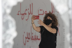 Lebanese director Carol Mansour uses her phone to film while wearing a face mask and standing by graffiti reading in Arabic 'death to the butcher leaders', in the center of the capital Beirut on June 1, 2020.