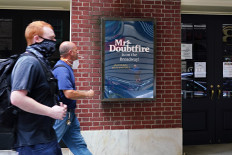 People wearing protective masks walk by Mrs. Doubtfire signage at Stephen Sondheim Theatre on June 29, 2020 in New York City. 