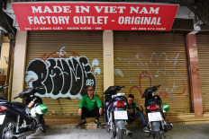 Ride-hailing drivers sit beside their motorcycles in front of a shop, closed due to COVID-19, in Hanoi, Vietnam, on July 2 last year.