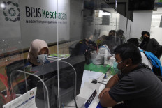 A Health Care and Social Security Agency (BPJS Kesehatan) official serves a policyholder from behind a glass screen on July 2, 2020, at the agency's representative office in Central Jakarta.
