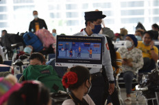 A security guard holding a placard reminding people of social distancing walks past Philippine overseas workers who were quarantined for weeks after returning home as they wait for flights back to their home cities around the country, at Manila's international airport on May 28, 2020. 