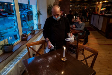 This file photo taken on May 15, 2020 shows
a waiter wearing a face mask sprays disinfectant on a table at Pepenero, an Italian restaurant in Berlin’s Prenzlauer Berg district, as lockdown measures were eased and cafes and restaurants were allowed to reopen amid the novel coronavirus COVID-19 pandemic. 