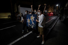 In this picture taken on July 9, 2020, people pose with the artwork 'Narcissi' created by Masako Hirano outside Same gallery after a man (left) took the painting during a stealable art exhibition in Tokyo. 