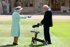 Britain's Queen Elizabeth II uses the sword that belonged to her father, George VI as she confers the Honour of Knighthood on 100-year-old veteran Captain Tom Moore at Windsor Castle in Windsor, west of London on July 17, 2020.
