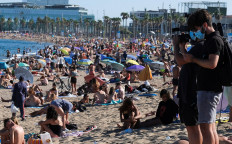 Journalists record as people enjoy the sunny weather at the Barceloneta beach, after Catalonia's regional authorities and the city council announced restrictions to contain the spread of the coronavirus disease (COVID-19) in Barcelona, Spain July 19, 2020. 