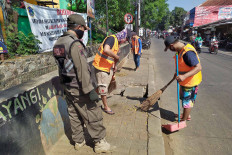 A Public Order Agency (Satpol PP) officer supervises three men as they sweep a sidewalk at Ciracas Market in East Jakarta on July 17. The three were obligated to take part in the act of community service after violating COVID-19 health protocols. - JP/P.J. Leo