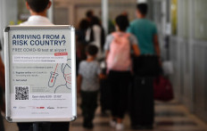 People queue near an information board promoting free COVID-19 tests for travellers arriving at the Berlin-Schoenefeld airport in Berlin, on July 31, 2020. 