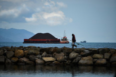 Heavy-laden: A man returns from fishing as a tugboat pulling a coal barge passes by in Banda Aceh, Aceh, on April 26, 2020.