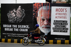 A motorcyclist rides past a billboard displaying a picture of Indian Prime Minister Narendra Modi (center) and messages on Indian-administered Kashmir along on a street in Islamabad on August 4, 2020 ahead of the Yaum-i-Istehsal or Day of Exploitation on August 5, on the first anniversary after India scrapped Muslim-majority region Kashmir's semi-autonomous status and imposed a major security clampdown.