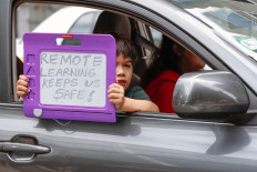 A kid holds a sign from a protester's car as it drives in the Occupy City Hall Protest and Car Caravan hosted by Chicago Teachers Union in Chicago, Illinois, on August 3, 2020. 