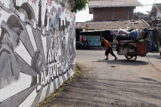 An informal waste sorter walks past a COVID-19-themed mural in Rempoa, South Jakarta, on Aug. 2. Jakarta accounts for 19.7 percent of the country’s COVID-19 cases, behind only East Java in its provincial tally. JP/Seto Wardhana
