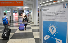 Travelers walk past an information board about the free of charge coronavirus testing at Munich airport on August 8, 2020.