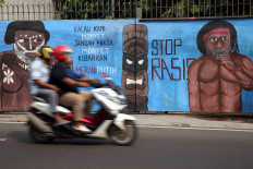 A motorcycle passes a mural with the words "If we're monkeys, don't force monkeys to fly the Indonesian flag."