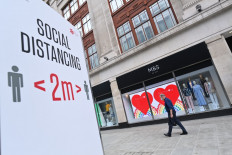 A shopper wearing a facemask as a precaution against the spread of the novel coronavirus walks past a store of the clothing and food retailer Marks and Spencer in central London on August 18, 2020 with social distancing advice displayed on the high street. 