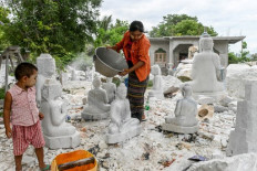 This photo taken on June 21, 2020 shows a woman washing dust off a marble statue in Sagyin village in Madaya township, about 46km from Mandalay. - Faces covered in white dust and chisels in hand, marble sculptors in Myanmar say the hills that have given them a livelihood for generations are disappearing, as large companies reap the rewards of the prized white rock. 