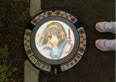 A passerby stands next to an illuminated manhole cover with designs of popular animation character from 'The Melancholy of Haruhi Suzumiya', on the street in Tokorozawa, near Tokyo, Japan, on August 19, 2020. 