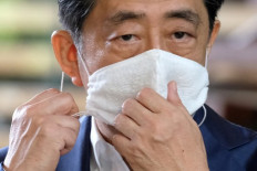 Japan's Prime Minister Shinzo Abe takes off his face mask prior to making a short speech to the media upon his arrival at the prime minister's office on August 24, 2020. - Abe earlier in the day returned to hospital on August 24 for more medical checks, a government spokesman said, a week after a first visit that fuelled growing speculation about his health.