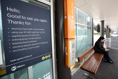 A person wearing a face mask sits at a bus stop next to posted safety guidelines on the first day of New Zealand's new coronavirus disease (COVID-19) safety measure that mandates wearing of a mask on public transport, in Auckland, New Zealand, August 31, 2020.  