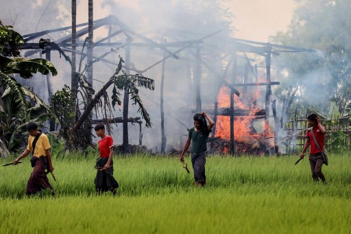 In this file photo taken on Sept. 7, 2017, unidentified men carry knives and slingshots as they walk past a burning house in Gawdu Tharya village near Maungdaw in Rakhine state in northern Myanmar. Myanmar's military has sought to undermine the confessions of two soldiers who said they were ordered to 