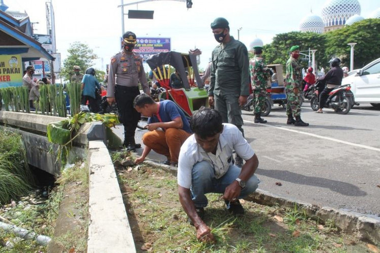 Local residents in Lhokseumawe, Aceh, who violate COVID-19 health protocols are ordered to clean a city park by pulling the weeds by local authorities on Sept. 14.