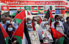 Demonstrators carrying Palestinian flags stand before a banner showing the flags of Arab League member states with Arabic text reading, “History will glorify but those faithful to Palestine and its cause,” during a protest against decisions by the United Arab Emirates and Bahrain to normalize relations with Israel, in the city of Nablus in the occupied West Bank on Sept. 15, 2020.