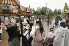 People wearing face masks take pictures in front of the new section of Tokyo Disneyland with the theme of film 'Beauty and the Beast' which is set to open on September 28, in Urayasu near Tokyo on September 25, 2020.
