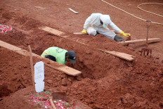Daily grind: One man digs a grave at the COVID-19 burial ground at Pondok Ranggon public cemetery in East Jakarta, on Monday, while another worker wearing personal protective gear helps him. The latter was originally tasked with carrying the bodies of COVID-19 victims, but he was needed to help the gravediggers, who have been under pressure due to the large number of burials.