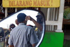 A Public Order Agency (Satpol PP) officer puts a face mask on a man during a security operation in Depok, West Java, on Sept 23. A joint security task force punishes anyone caught not wearing a mask by making them wear an orange vest and recite state ideology Pancasila. JP/PJ Leo