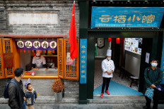 Restaurant workers wear face masks as people walk in the tourist area surrounding Houhai Lake during Chinese National Day holidays in Beijing, China, Oct. 2, 2020. 