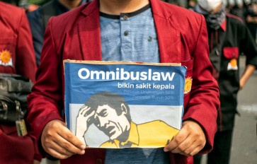 A student protester holds up a poster based on the packaging design of a headache medicine on Oct. 8, 2020, during a demonstration on Jl. M.H. Thamrin in Central Jakarta. The poster reads: “The omnibus law causes headaches, environmental damage, workers’ oppression.”