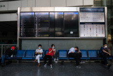 People wear face masks as they sit under a flight departure board at the in-town check-in for Hong Kong's international airport on July 16, 2020.