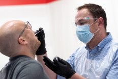 A handout picture released by LHR Airports Limited on October 20, 2020 shows a nurse swabbing the throat of a traveler as he administers a COVID-19 test in Heathrow Airport in west London. 