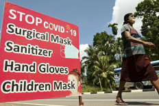 A woman wearing a facemask walks past a display featuring health and safety measures against the spread of the Covid-19 Coronavirus on a street in Piliyandala, a suburb of Sri Lanka's capital Colombo on October 23, 2020. 