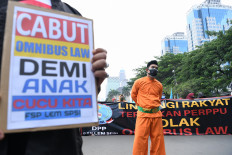Protesters hold banners during a demonstration against the Job Creation Law on Jl. Medan Merdeka Barat in Jakarta on Oct. 28, 2020. The poster in the foreground reads, "Revoke the omnibus law for our children and grandchildren."