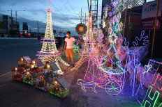 This photo taken on October 6, 2020 shows a worker standing beside lanterns and lit ornaments, including several shaped in the likeness of the Eiffel Tower, for sale during the festive season at a shop in San Fernando town in Pampanga province. 