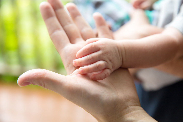 An illustration of baby's hand on top of mother's hand.