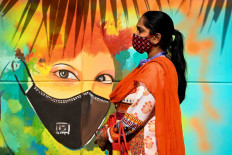 A woman wearing a facemask as a preventive measure against the Covid-19 coronavirus walks past a mural in New Delhi on November 23, 2020. 