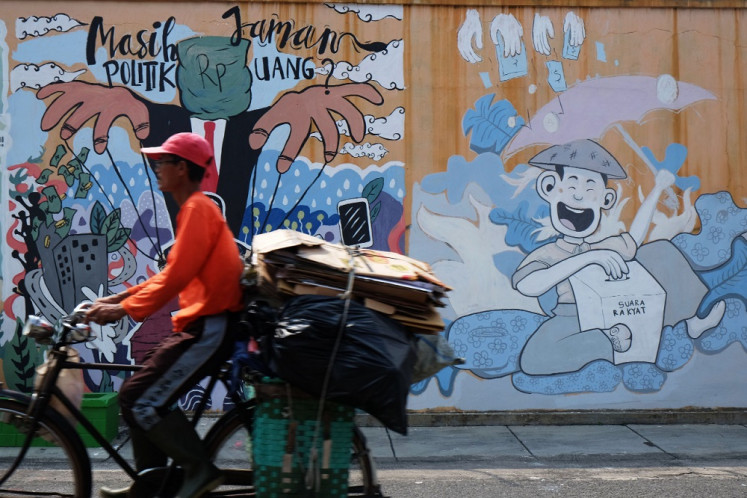 A cyclist rides on July 22, 2020, past a mural in Surakarta, Central Java, that calls on people to reject vote-buying.