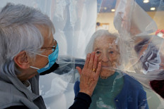 Marie-Paule and Marie-Josephe interact with their mother Colette, 97 years old, behind a removable plastic sheet inside a bubble structure which allows families to give hugs without risk of contamination or transmission of COVID-19, installed in the refectory of the Residence du Carre d'Or retirement home at Jeumont Hospital, as the coronavirus disease outbreak continues in France, on December 4, 2020. 