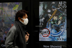A man wearing a protective mask amid the coronavirus disease (COVID-19) outbreak walks past a poster for an animated movie 'Demon Slayer' in front of a movie theater in Tokyo, Japan, on December 13, 2020. 