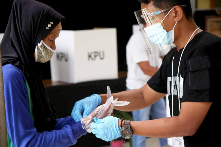 A poll worker (right) helps a woman put on a plastic glove before she casts her ballot at a polling station in Tapos, Depok, West Java, on Dec. 9, 2020. Poll workers enforced strict health protocols on voting day for the Depok mayoral election, requiring voters to wear gloves and face masks, among other precautions. JP/PJ Leo