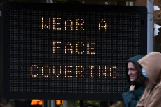 Pedestrians walk past an electronic sign that advises people to wear a face covering because of the coronavirus pandemic in London on December 16, 2020. - London on Wednesday moved into the highest level of coronavirus restrictions in an effort to control rising infection rates, dealing another blow to hospitality venues before Christmas. The British capital's move into 