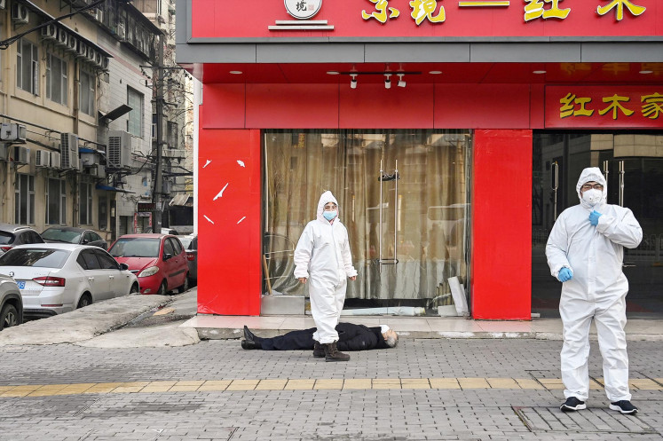 This photo taken on January 30, 2020 shows officials in protective suits checking on an elderly man wearing a facemask who collapsed and died on a street near a hospital in Wuhan. 