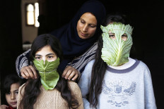A Palestinian mother entertain her children with makeshift masks made of cabbage as she cooks in Beit Lahia in the northern Gaza Strip on April 16, 2020 amid the coronavirus COVID-19 pandemic. AFP/Mohammed Abed