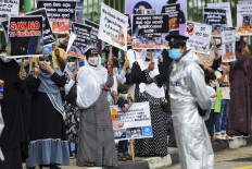 In this file photo taken on December 31, 2020 a policeman stands guard as protesters hold placards during a demonstration against the government policy of forced cremations of Muslims who died of the Covid-19 coronavirus, outside a cemetery in Colombo. Sri Lanka's government stuck on January 8, 2021 with its policy of forced cremations of coronavirus victims, rejecting international pleas and recommendations from its own experts to allow the Muslim minority to bury their dead.