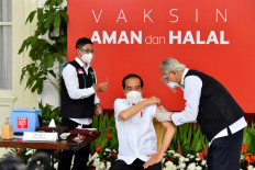 This handout photo taken and released on January 13, 2021 by the Presidential Palace shows Indonesian President Joko Widodo (center) receiving the country's first Covid-19 vaccine jab.