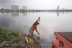 A worker takes water from Pluit Reservoir in North Jakarta on Jan. 22, 2021, to mix construction materials as he and other workers work to repair a drainage system. 